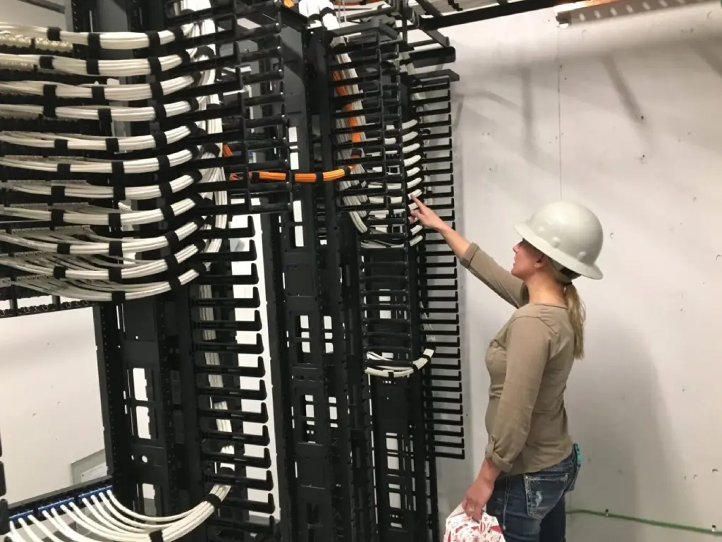 A woman in a hard hat is looking at some wires.