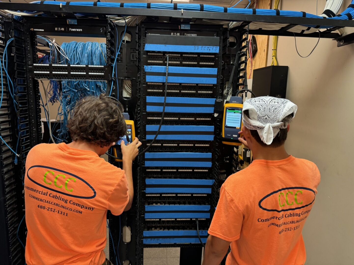 Two men in orange shirts working on a rack of wires.